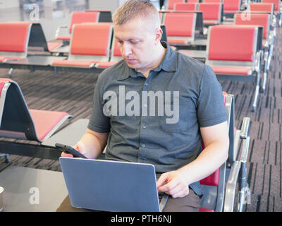handsome middle age man working at airport lounge with laptop and smartphone in hand. mobile office concept. front view close shot Stock Photo
