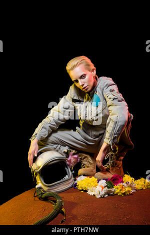 stylish cosmonaut in spacesuit with flowers and helmet sitting on planet Stock Photo