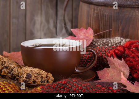 Steaming cup of coffee and raisin cookie on a colorful blanket with autumn leaves and rustic wooden background Stock Photo