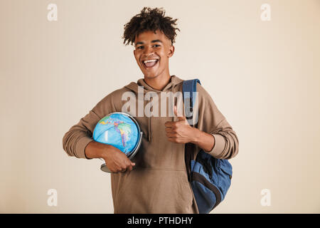 Portrait of a smart young afro american man dressed in hoodie carrying backpack isolated, holding earth globe Stock Photo