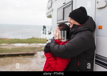 Affectionate couple in warm clothing hugging outside motor home Stock Photo