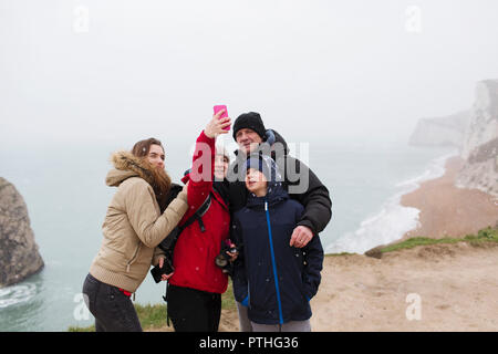 Family with camera phone taking selfie on cliff overlooking ocean Stock Photo