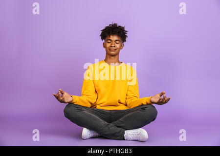 Portrait of relaxed african american boy sitting in lotus pose and meditating with closed eyes isolated over violet background Stock Photo