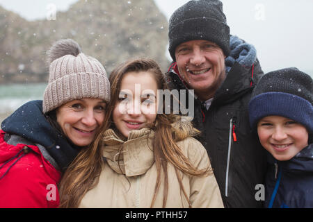 Snow falling over smiling family posing in warm clothing Stock Photo