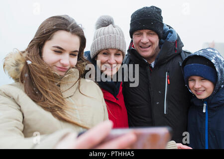 Snow falling on smiling family taking selfie Stock Photo