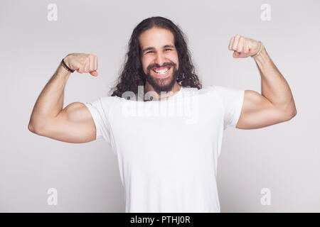 Portrait of strong bodybuilder man in white t-shirt with long wavy hair and beard, standing, posing and looking at camera with proud toothy smile. ind Stock Photo