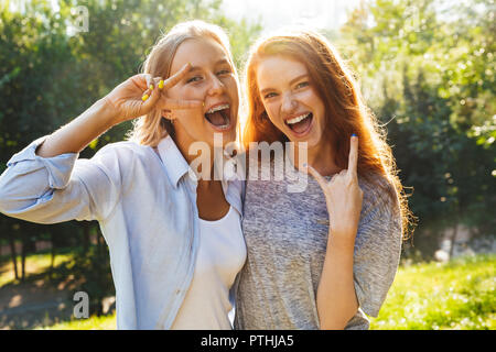 Two happy youg girls having fun at the park, showing peace gesture ...