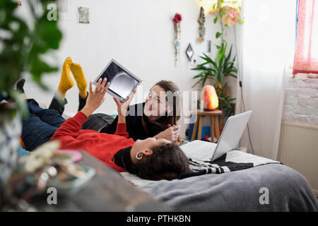 Young women friends relaxing, using digital tablet and laptop on bed Stock Photo
