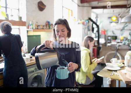 Young woman pouring hot water into teapot in apartment kitchen Stock Photo