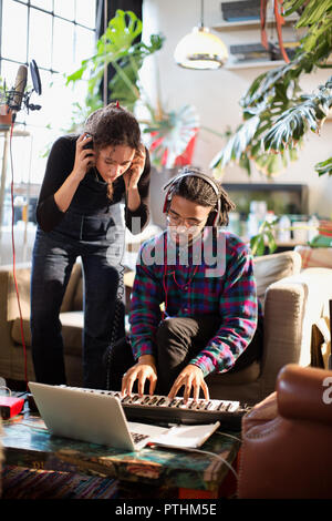 Young man and woman recording music, playing keyboard piano in apartment Stock Photo