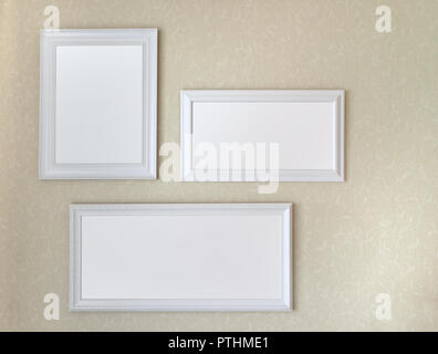 Three white wooden frames hanging on soft yellow wall mock up template. Stock Photo