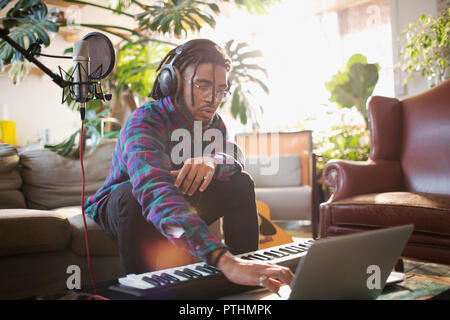 Young male musician recording music, using laptop and keyboard piano Stock Photo