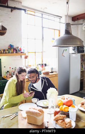 Young couple with smart phone enjoying breakfast in apartment kitchen Stock Photo