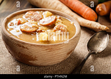Wooden bowl of split pea soup with sausage, bacon and potatoes Stock Photo