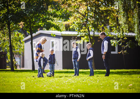 The theme family outdoor activities. big friendly Caucasian family of six mom dad and four children playing football, running with the ball on lawn, g Stock Photo