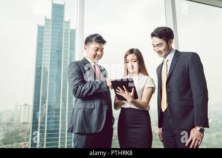 Portrait of businesspeople standing near the window looking at digital tablet Stock Photo