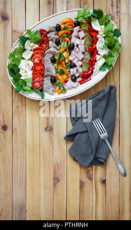 A popular dish of American cuisine - Cobb salad, consisting of greens, eggs, tomatoes, cheese, meat products, stacked in rows on a wide dish and poure Stock Photo