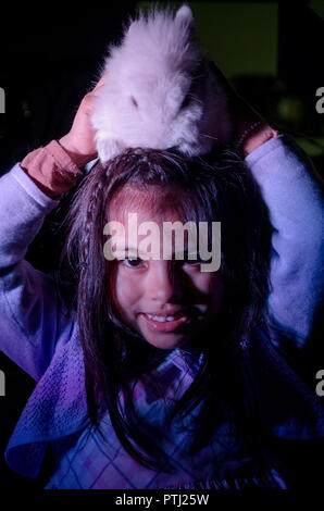 Happy little girl with her pet bunny on her head on dark background Stock Photo