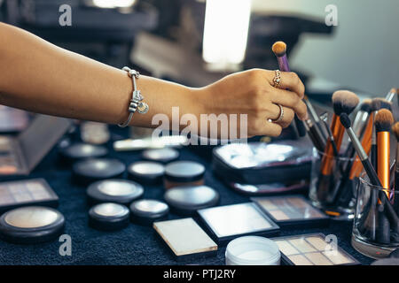 Makeup artist picking up a brush for makeup. Makeup brushes and foundation shades arranged on table in a makeup room. Stock Photo