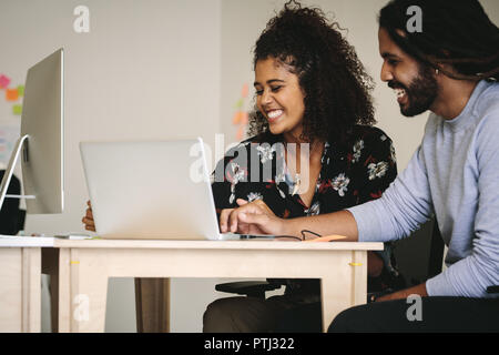 Business partners sharing ideas sitting at the desk with laptop computer. Happy business colleagues in office working on a project together. Stock Photo