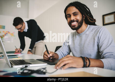 Happy businessman writing on a digital writing pad connected to a laptop computer. Creative business colleagues working in office using modern technol Stock Photo