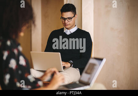Businessman and woman working on their laptops sitting on chairs in office. Creative business teammates working on laptops in office. Stock Photo