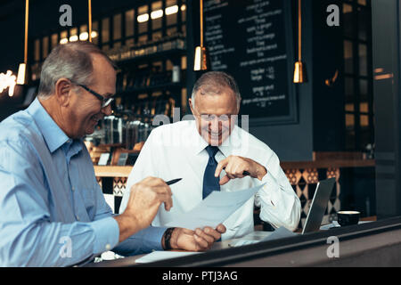 Happy senior business people talking over few reports at cafe. Two business partners reviewing contract papers at a restaurant. Stock Photo