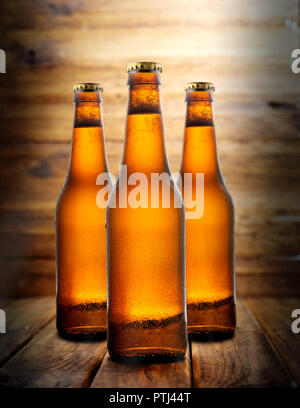 Three delicious beer bottles on top of a wooden table and wood background, bar counter, with lots of water droplets Stock Photo