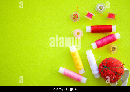 Multicolored thread coils red pink yellow white and measuring tape on green background. Sewing supplies and accessories for needlework, stitching, emb Stock Photo