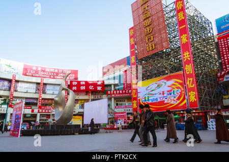 Kashgar, Xinjiang, China : Uyghur people walk past a modern shopping mall in the modern city of Kashgar. Stock Photo