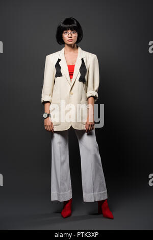 fashionable young woman in stylish jacket and bell-bottoms on grey Stock Photo