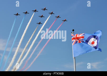 RAF, Royal Air Force Red Arrows jet planes flying over RAF ensign flag. British air display team flypast over Union Jack flag. Blue sky Stock Photo