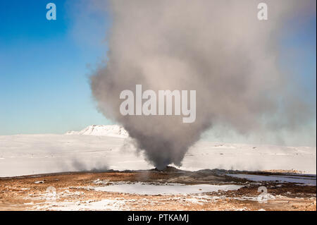 Giant smoke plume rises from a fumarole in Hverir geothermal area, Iceland. Winter landscape, snow covered mountainside against blue sky background Stock Photo