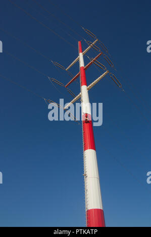 View from below of a red and white high voltage tower with blue sky as background Stock Photo