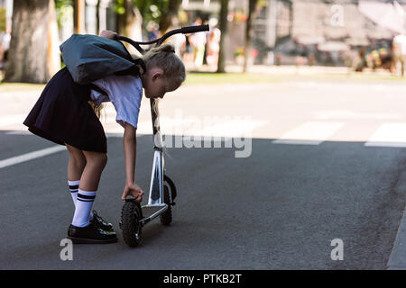 back view of cute little child with backpack fixing scooter on street Stock Photo