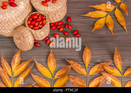 Rose hips in a basket and yellow leaves on a wooden surface, concept of autumn background Stock Photo