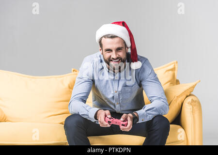 smiling bearded man in santa hat playing video game with joystick on grey Stock Photo