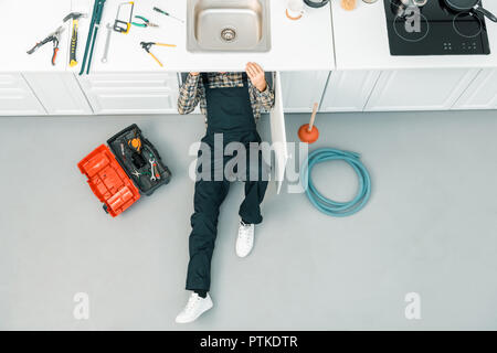 high angle view of plumber lying on floor and checking sink in kitchen Stock Photo