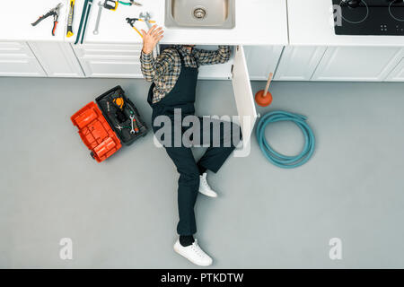 high angle view of plumber lying on floor, checking sink and taking tools in kitchen Stock Photo