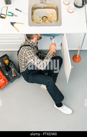 high angle view of plumber repairing sink with adjustable wrench in kitchen Stock Photo