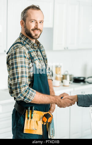 smiling handsome plumber and customer shaking hands in kitchen Stock Photo
