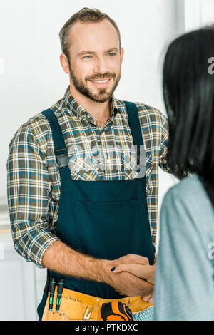 smiling handsome plumber and client shaking hands in kitchen Stock Photo