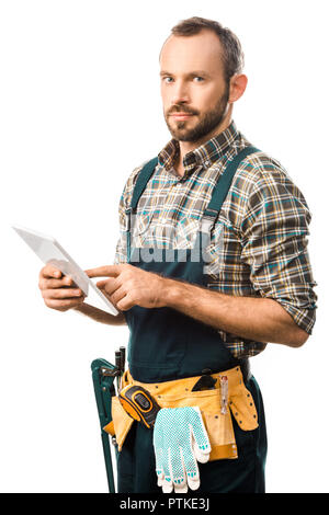 handsome plumber with tool belt using digital tablet isolated on white and looking at camera Stock Photo