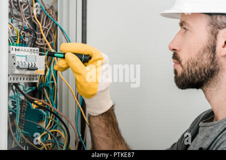side view of handsome electrician repairing electrical box and using screwdriver in corridor Stock Photo