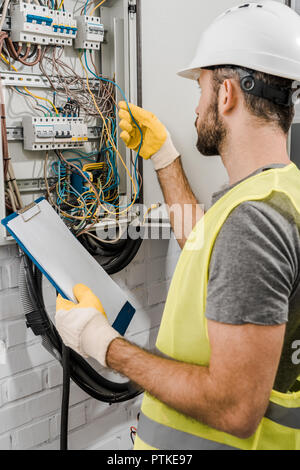 electrician holding clipboard and checking wires in electrical box in corridor Stock Photo