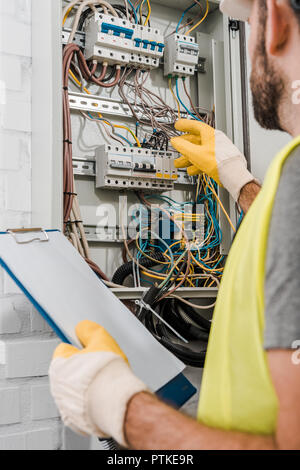 cropped image of electrician holding clipboard and inspecting electrical box in corridor Stock Photo
