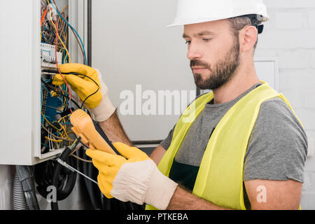 handsome electrician checking electrical panel with multimetr in corridor Stock Photo