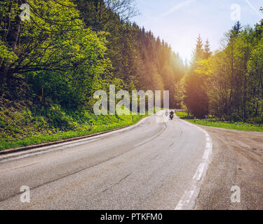 Bikers on mountainous highway, biker on the road in sunset light riding on curve road pass across Alpine mountains, extreme lifestyle, freedom concept Stock Photo