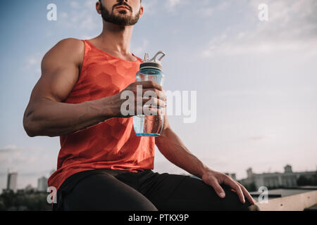 cropped image of sportsman holding sport bottle of water on roof Stock Photo