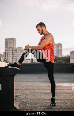 side view of handsome sportsman stretching legs on roof Stock Photo